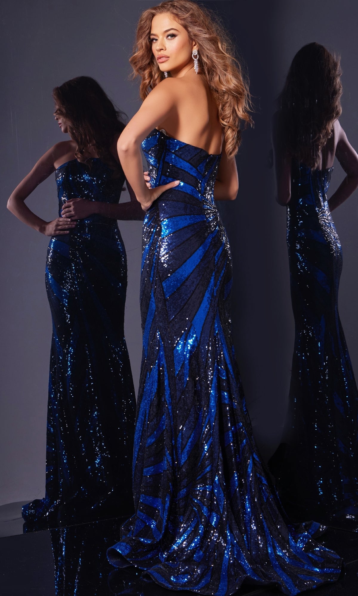 A woman models the Jovani 40765 Long Prom Dress, a form-fitting, strapless, floor-length blue and black sequin gown, standing before a mirror to display its back and side views.